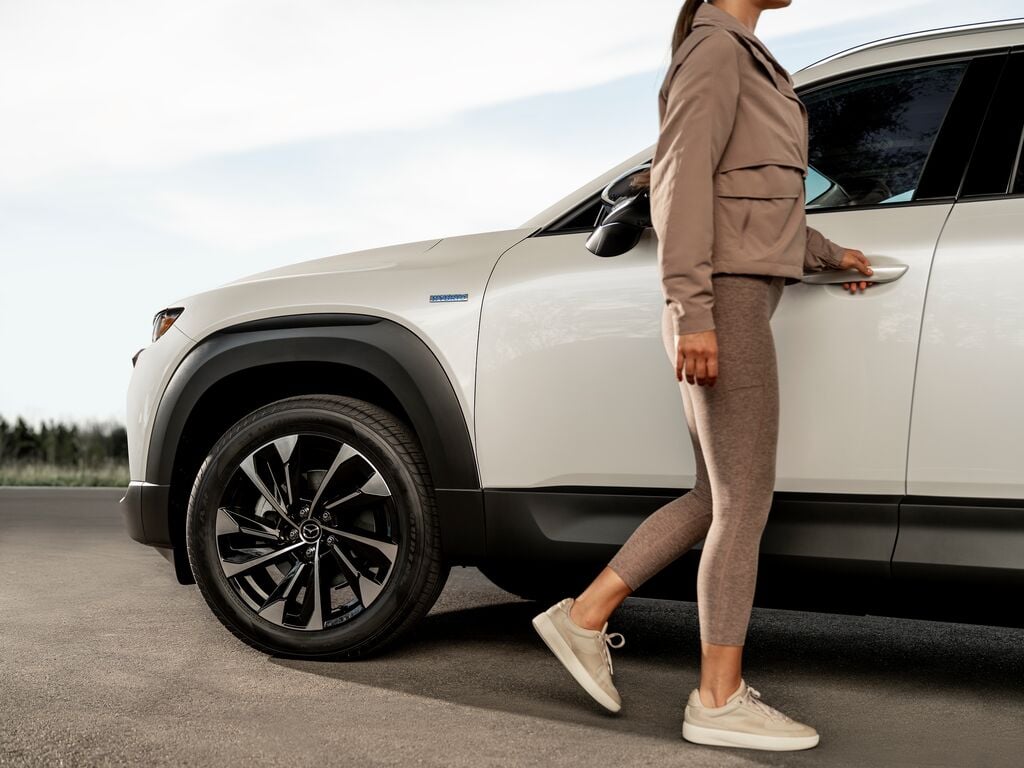 Logo Hybride du Mazda CX-50 hybride avec une femme qui va ouvrir la porte.